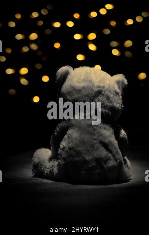 Photo verticale d'un ours en peluche vu de l'arrière sous les projecteurs contre les lumières jaunes du bokeh Banque D'Images