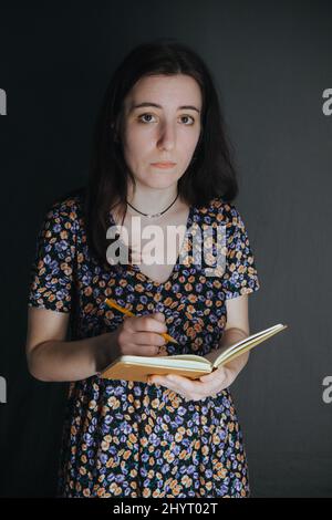 une jeune femme arménienne ukrainienne prend des notes avec un stylo dans son carnet sur fond gris Banque D'Images