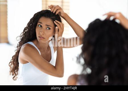 Inquiète jeune femme vérifiant ses racines de cheveux à la maison, ayant Dandruff problème Banque D'Images