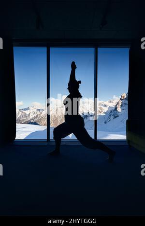 Jeune femme silhouette faisant méditation yoga guerrier virabhadrasana pose avec dans la chambre avec vue panoramique d'un beau paysage de montagne. Healt Banque D'Images