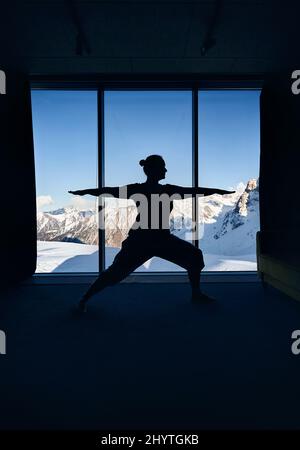 Jeune femme silhouette faisant méditation yoga guerrier virabhadrasana pose avec dans la chambre avec vue panoramique d'un beau paysage de montagne. Healt Banque D'Images