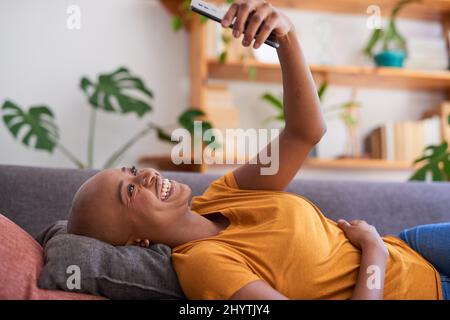 Une jeune femme se trouve sur le canapé et regarde son téléphone portable Banque D'Images