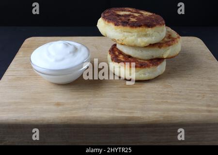 petit-déjeuner fromage fromage crêpes cheesecakes sur un plateau en bois avec sauce à la crème aigre blanche. Plat de petit déjeuner sain russe fromage cottage nourriture saine Banque D'Images