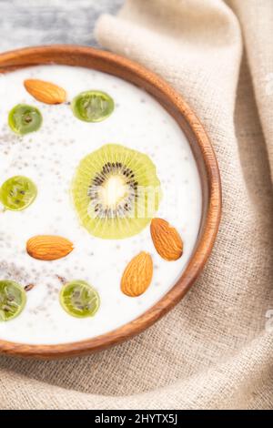 Yaourt au kiwi, à la groseille, au chia et aux amandes dans un bol en bois sur fond en bois gris et linge de maison. Vue de dessus, gros plan, mise au point sélective. Banque D'Images