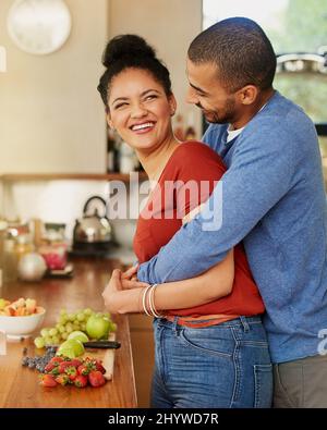 Faire des choix sains en couple. Photo d'un jeune homme qui embrasse sa femme pendant qu'elle prépare un en-cas sain à la maison. Banque D'Images