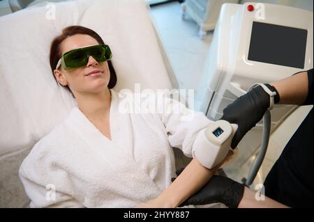 Vue aérienne d'une belle femme d'âge moyen du Caucase subissant une procédure d'épilation sur les mains dans un salon de beauté. Soins du corps. Épilation au laser. Epila Banque D'Images