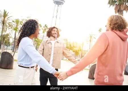 Jeune groupe d'amis en cercle tenant les mains à l'extérieur. Étreinte les gens qui rient. Culture de la jeunesse et mode de vie de la ville Banque D'Images