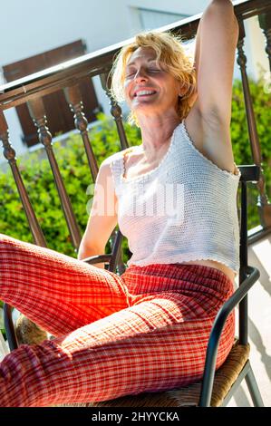 portrait d'une jeune femme blonde caucasienne mûre se détendant à la maison sur le porche assis dans une chaise à bascule. Concept de style de vie. Banque D'Images