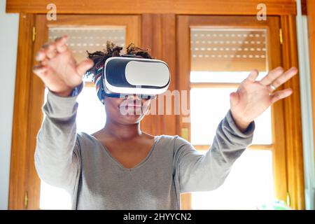 Portrait d'une jeune femme noire active qui teste un simulateur de réalité virtuelle dans une pièce à la maison. Technologies et concepts de style de vie. Banque D'Images