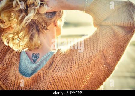 Vue arrière d'une jeune femme blanche blonde avec un tatouage dans est nape à l'extérieur dans un secteur de plage dans une journée ensoleillée. Plage de Berria, Cantabrie, Espagne, Europe. Banque D'Images