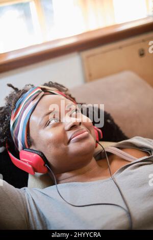 Portrait d'une jeune femme noire écoutant de la musique avec un casque d'intérieur allongé sur un canapé. Concept de style de vie. Banque D'Images