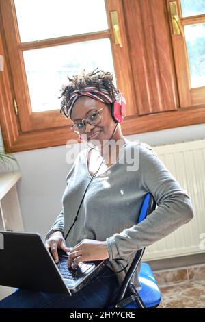 Jeune femme noire avec une coiffure afro écouter de la musique avec des écouteurs à l'intérieur d'une maison. Concept de style de vie. Banque D'Images