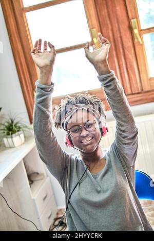 Jeune femme noire avec une coiffure afro écouter de la musique avec des écouteurs à l'intérieur d'une maison. Concept de style de vie. Banque D'Images