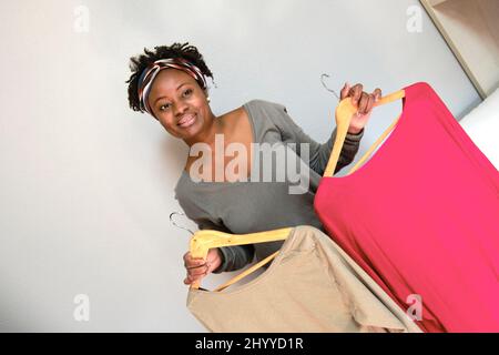 Portrait d'une jeune femme noire avec une coiffure afro avec des vêtements sur cintres à l'intérieur à la maison. Concept de style de vie. Banque D'Images