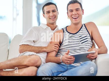 Chaque jour est spécial. Portrait d'un couple gay utilisant une tablette numérique tout en se relaxant sur le canapé à la maison. Banque D'Images