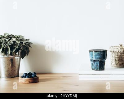 Concept minimaliste de l'intérieur de salon avec la maison en pot métallique, magazines, verre avec boisson et bleuets sur table en bois. Copier l'espace. T Banque D'Images