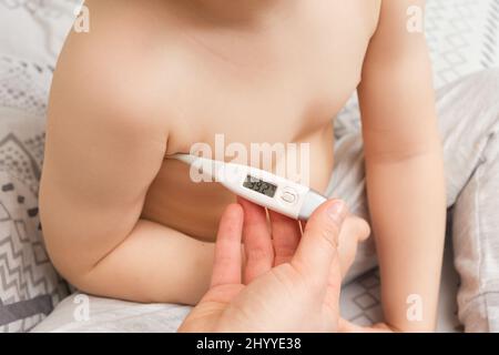 Une mère ou une infirmière mesure la température d'un garçon de 4 ans à l'aide d'un thermomètre électronique Banque D'Images