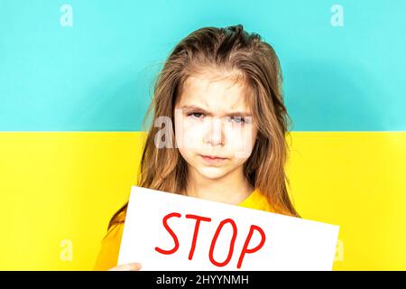 Le visage d'une fille qui pleure en gros plan. La fille tient une AFFICHE D'ARRÊT dans ses mains contre le fond du drapeau ukrainien. Arrêter la guerre en Ukraine Banque D'Images