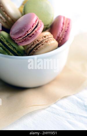 Macarons français dans un bol sur papier parchemin à la lumière naturelle Banque D'Images