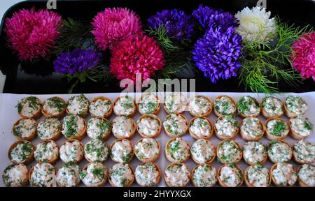 Des gobelets de cocktail remplis de salade de poulet, des hors-d'œuvre sur un plateau décoré de fleurs Banque D'Images