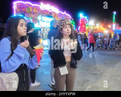 Distrait les femmes mangeant des frites et des gaufres debout lors d'une foire nocturne Banque D'Images