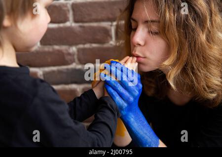 Une femme apaise un petit garçon, tient ses mains dans sa propre, peint en jaune et bleu des couleurs du drapeau ukrainien. Famille, unité, consolation. Soins Banque D'Images