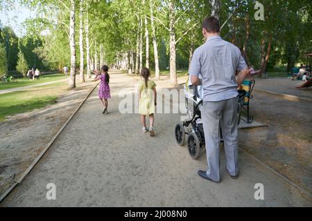 Une famille avec une poussette qui marche dans le parc un jour d'été, une famille le week-end. Un père heureux avec un bébé dans une poussette dans un parc d'été. Photo de haute qualité Banque D'Images