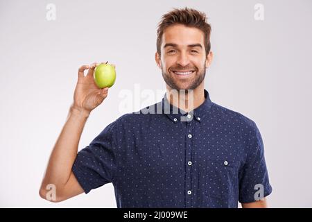 Le snack qui garde votre corps heureux. Portrait d'un beau jeune homme tenant une pomme et en train de mordre. Banque D'Images