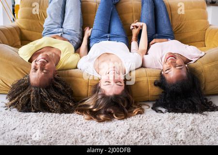 Trois copines les femmes souriantes au sofa rire bon. Les jeunes s'amusent ensemble à la maison. Banque D'Images