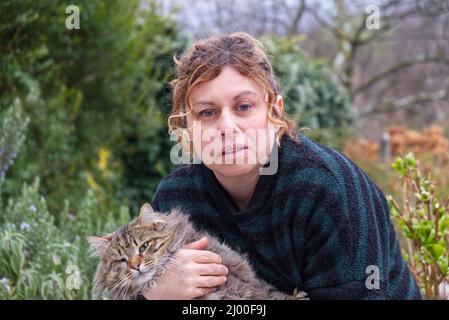 brunette femme de cinquante ans de race blanche avec un maillet vert rayé câline un chat Banque D'Images