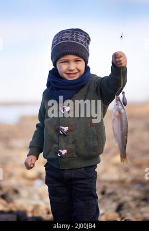 Regardez, c'est ma plus grande prise à ce jour. Portrait d'un petit garçon mignon tenant le poisson qu'il a attrapé. Banque D'Images