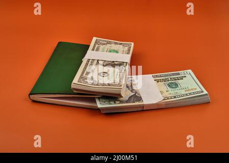 Carnet vert avec deux lots de dollars sur une table orange. Banque D'Images
