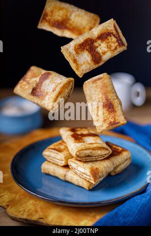 Crêpes avec le fromage cottage de remplissage tombent d'en haut sur une assiette, la lévitation. Gros plan. Banque D'Images