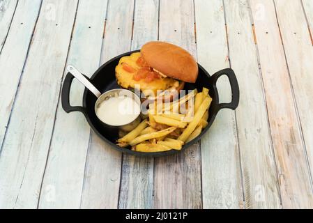 Hamburger servi dans une poêle à poignées noires avec une portion de pommes de terre maison, sauce et fromage cheddar fondu avec morceaux de tomate Banque D'Images