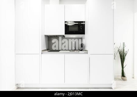 Cuisine au mobilier blanc avec four à micro-ondes noir, plaque vitrocéramique et évier à côté de la machine à café Banque D'Images