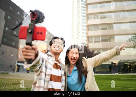 Des gens asiatiques blogging à l'extérieur. Selfie couple voyage heureux marcher touristes prenant photo avec le téléphone sur la ville rue panorama style de vie. Banque D'Images
