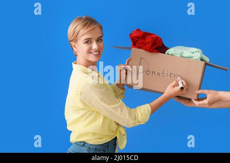 Jeune femme avec boîte écrivant des dons de mots sur fond bleu Banque D'Images