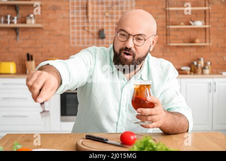 Homme chauve buvant de la bière et prenant le déjeuner dans la cuisine Banque D'Images