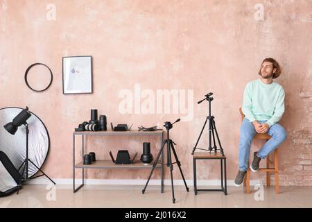 Jeune homme assis dans une chaise près du mur rose dans un studio photo moderne Banque D'Images