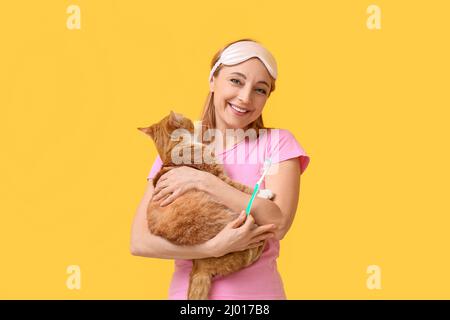 Belle femme mûre avec chat mignon se brossant les dents sur fond jaune Banque D'Images