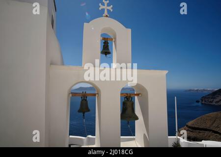 Trois cloches d'église et une croix religieuse sur le dessus à côté d'une église et une belle vue sur la mer égée à Santorin Banque D'Images