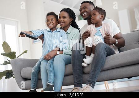 À la télé. Prise de vue sous angle d'une jeune famille affectueuse de quatre personnes regardant la télévision dans le salon de la maison. Banque D'Images