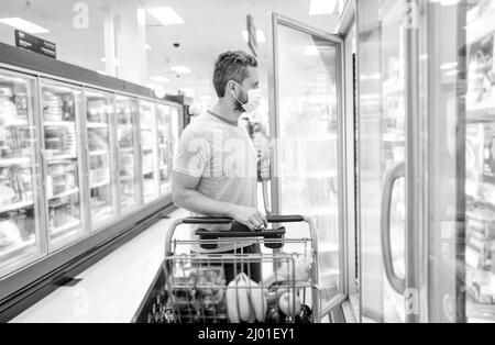 homme dans le masque de protection avec panier d'achat de nourriture à l'épicerie, shopping Banque D'Images