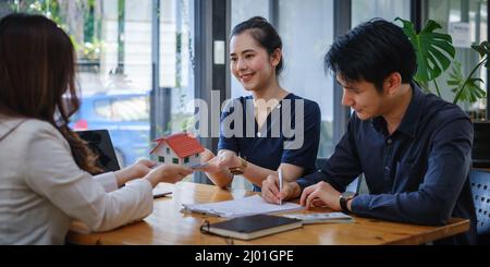 Le jeune couple décide avant de signer le contrat et le prix tandis que le courtier offre le prix exclusif. Concept immobilier. Banque D'Images