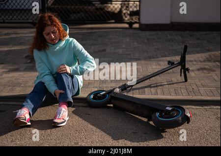 Une femme de race blanche est tombée d'un scooter électrique et a blessé sa jambe.Souffrant de douleur. Banque D'Images