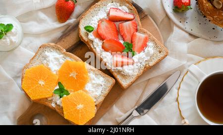 Toasts de petit déjeuner sains avec fruits frais, pain de wholegrain, fraises fraîches, oranges et fromage à la crème maison sur la table. Vue du dessus Banque D'Images