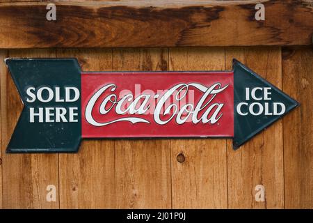 Vieux métal Coca Cola société de boisson non alcoolisée vendue ici glace froide flèche en forme de signe publicitaire affiché sur le mur de bois de planche. Banque D'Images