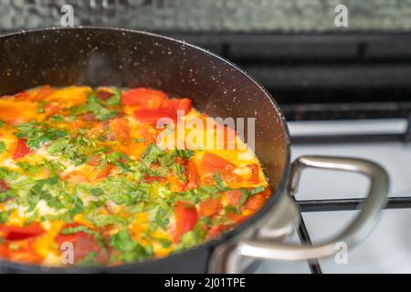 Oeufs frits avec légumes et herbes dans une poêle noire sur poêle blanche. Vue latérale Banque D'Images