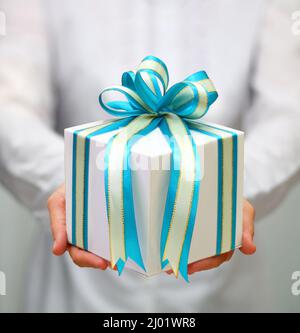 Gros plan de mains de femmes tenant une grande boîte cadeau enveloppée de ruban bleu. Banque D'Images