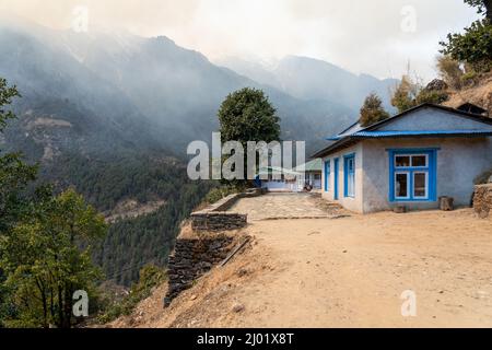 Un sentier traversant un petit village dans les montagnes de l'Himalaya qui sont couverts de fumée d'un feu de forêt à proximité. Banque D'Images